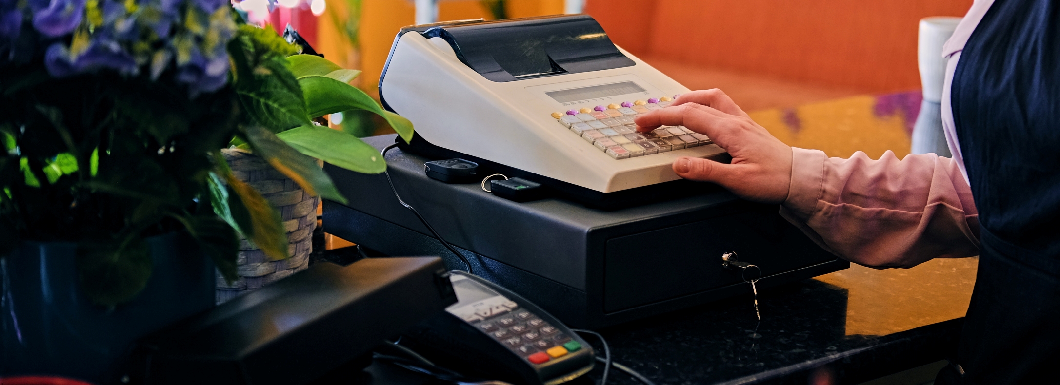 Redhead female flower seller using cash register in a market shop.